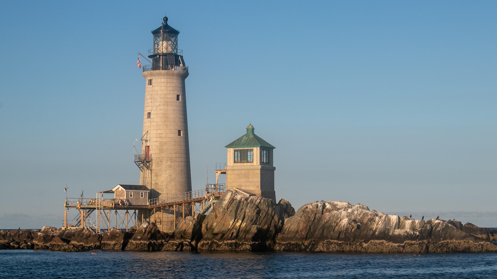 A lighthouse and a smaller building and pier on a rocky outcropping.