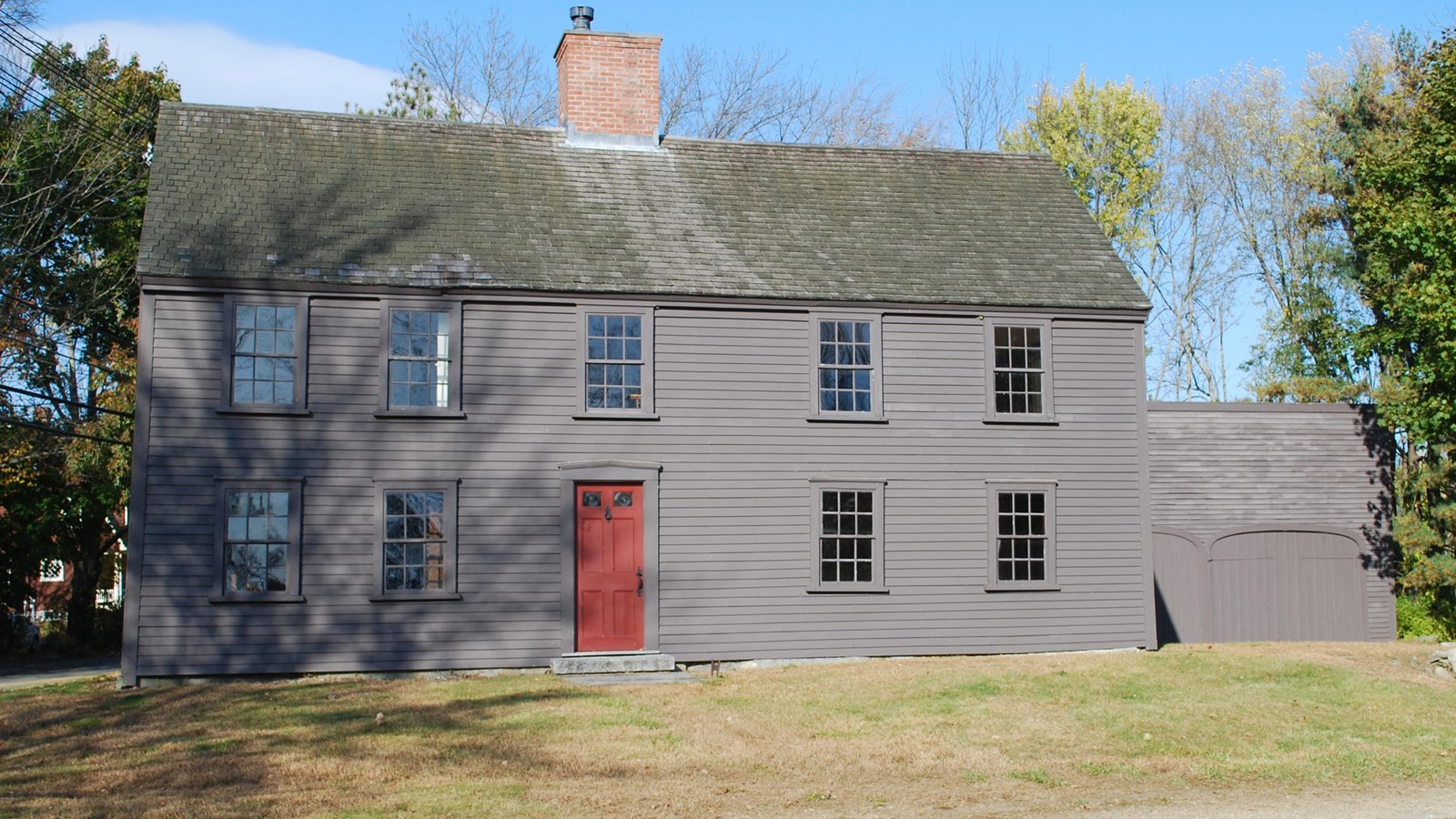 Two story wooden colonial house, dark gray wooden siding and a central chimney. 