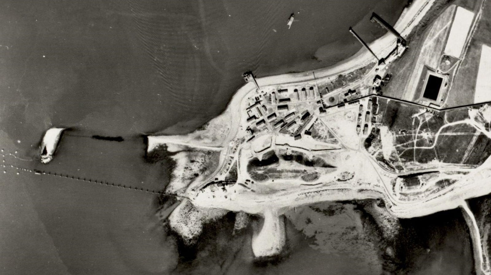 black and white aerial photo of part of the tip of an island, above a fort. 