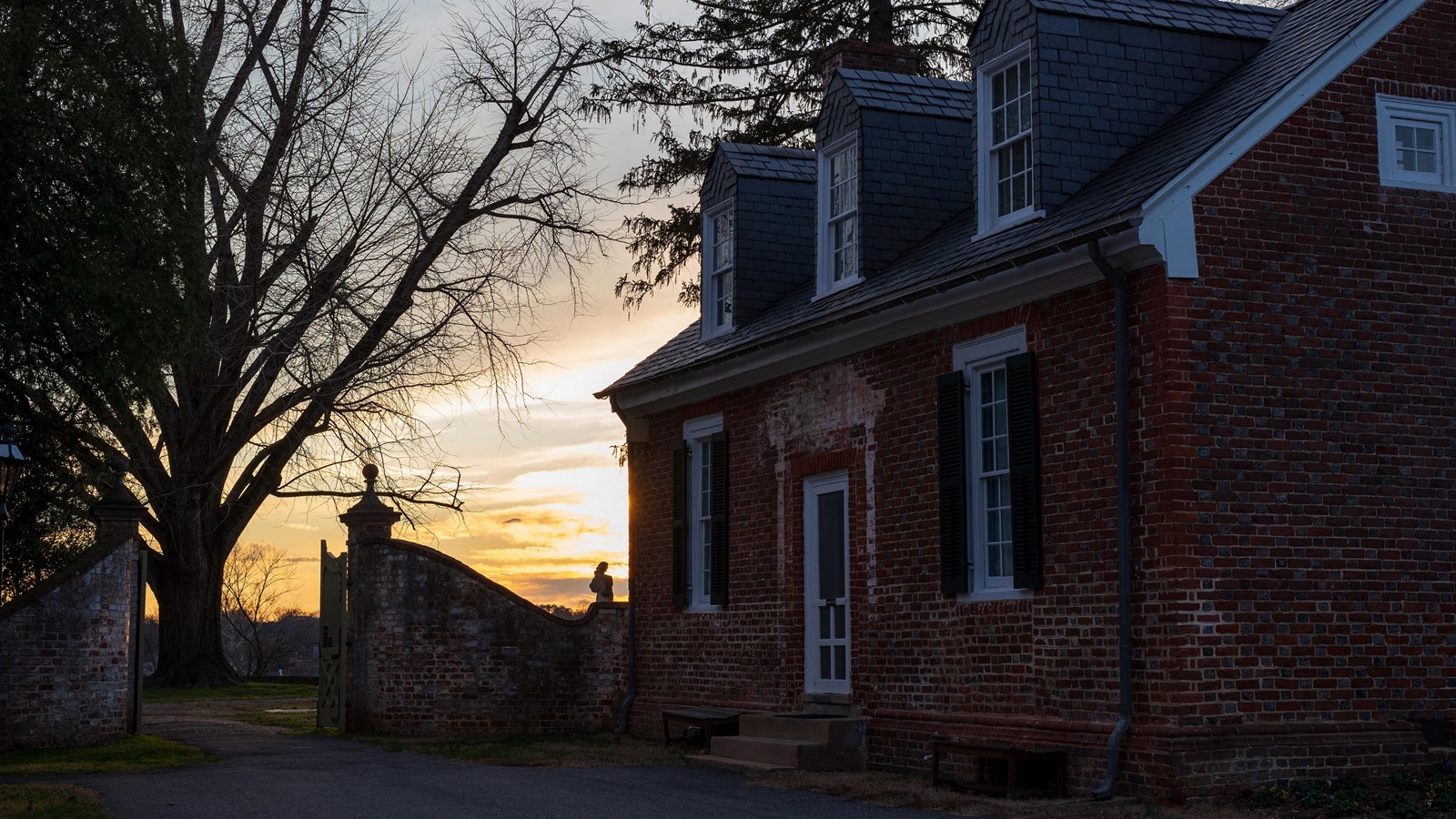 A brick, two story building next to a gate at sunset.