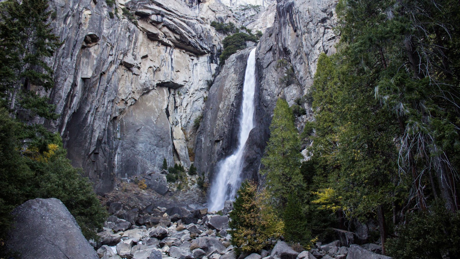 A tall waterfall flows strongly over a cliff and into boulders
