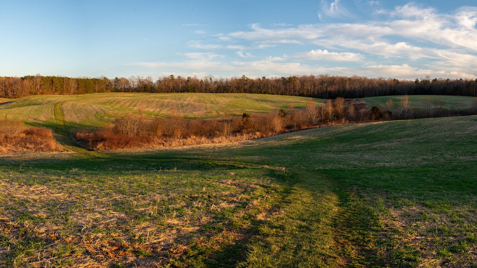 An open agricultural field with a light 1-inch layer of snow on sunny day.