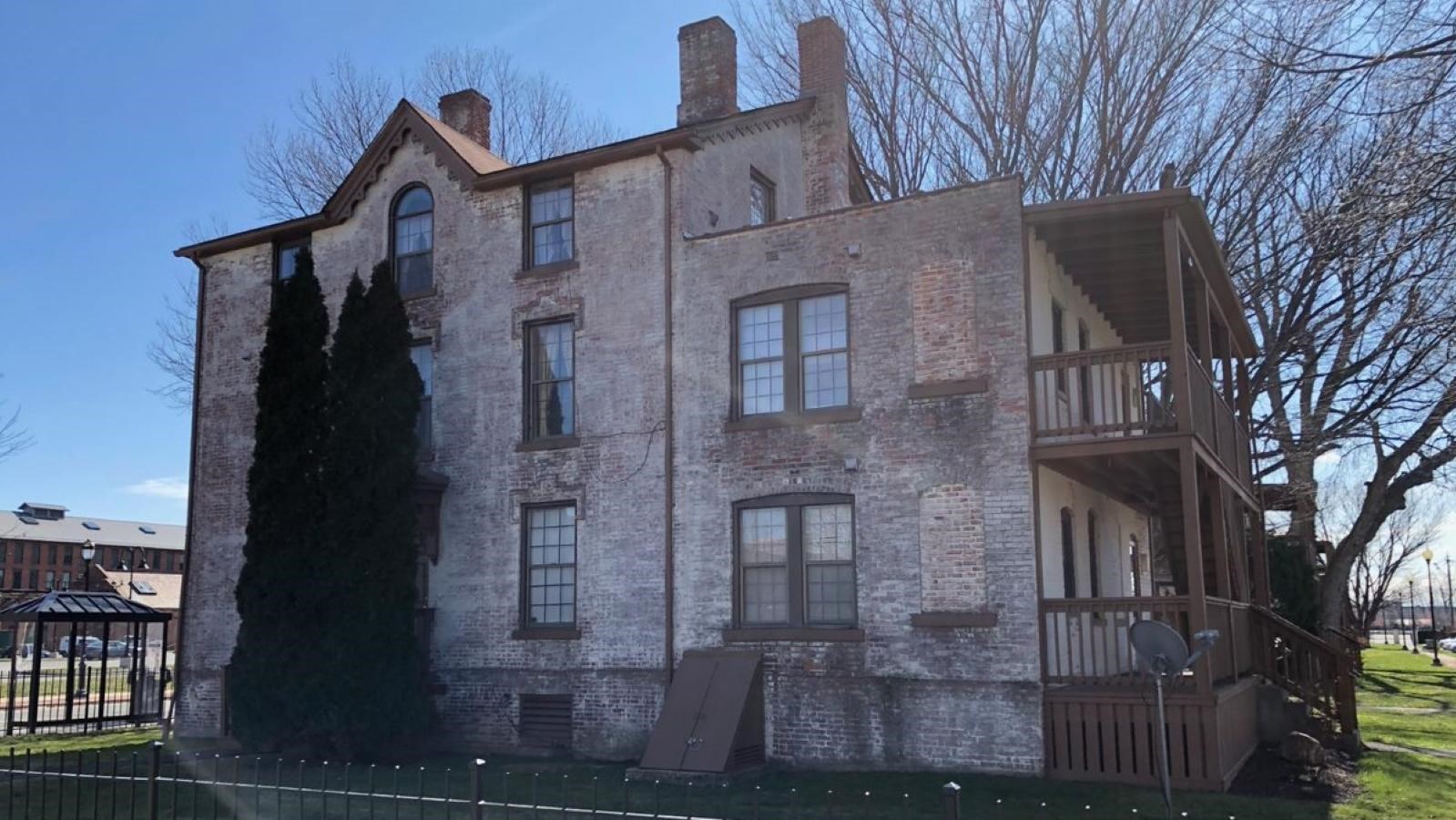 A house of red brick construction showing through white paint with an exterior stairwell.