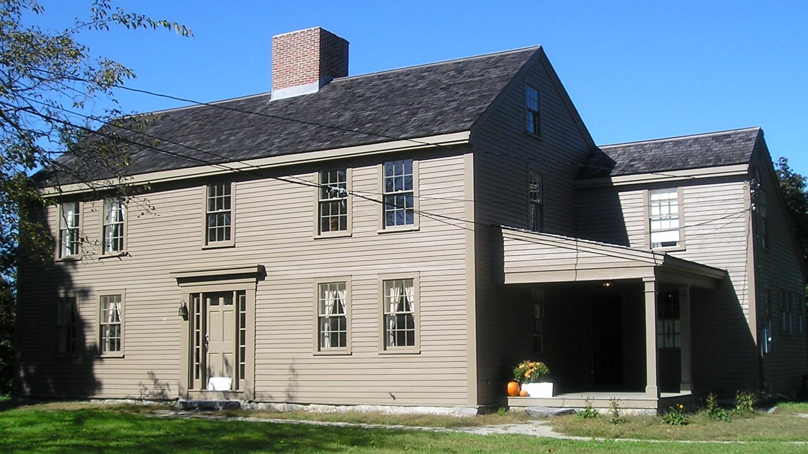 Two story wooden colonial house, dark brown wooden siding and a central chimney. 