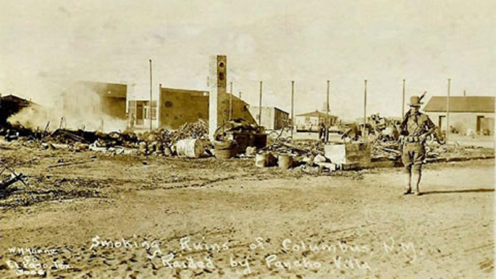soldier in broad hat stands in front of rubble of destroyed buildings