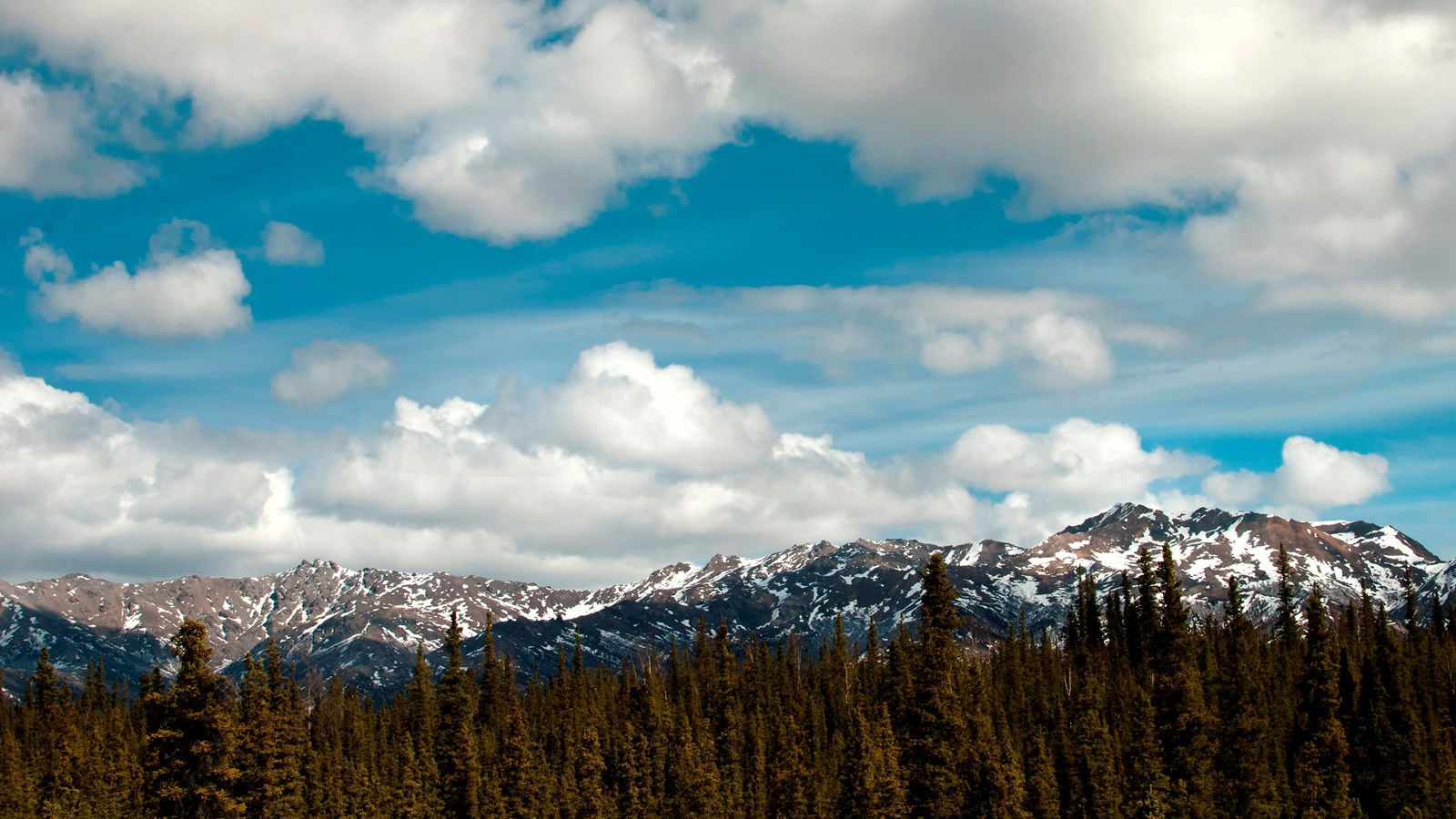 puffy white clouds in a blue sky over a ridge dappled with snow