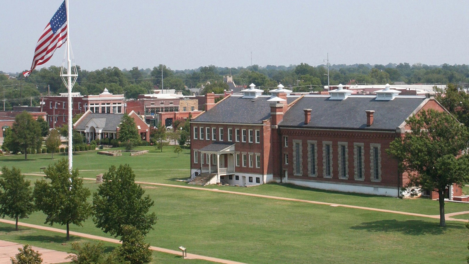 Tall flagpole with large US flag stands in parade ground in front of visitor canter.