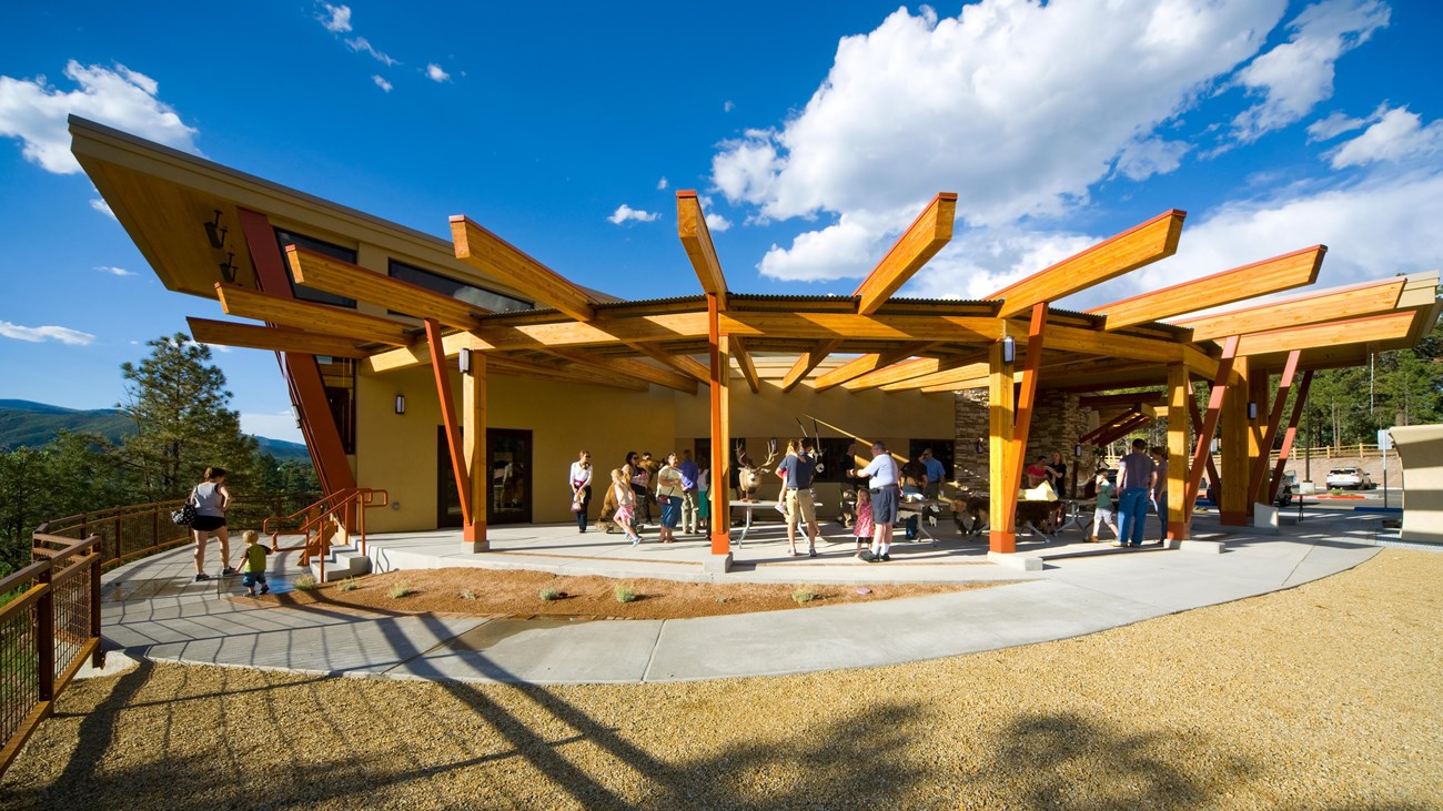 People mill around a modern building with wood beams radiating out from the roof.