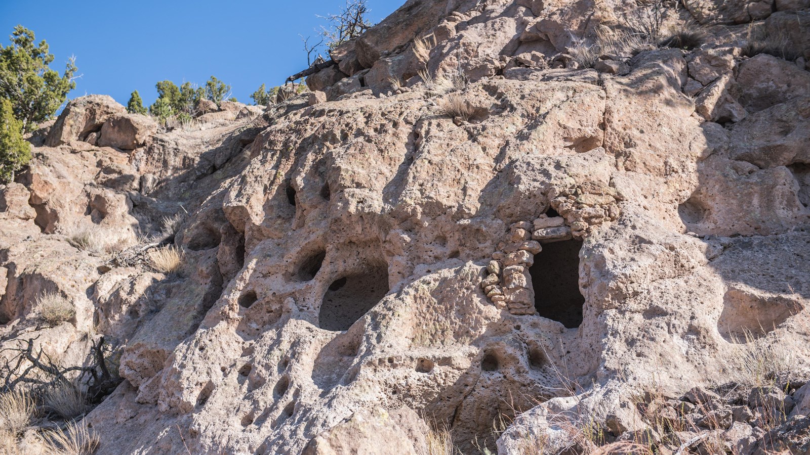 Natural and man-made niches in a cliff wall sit under a blue sky.