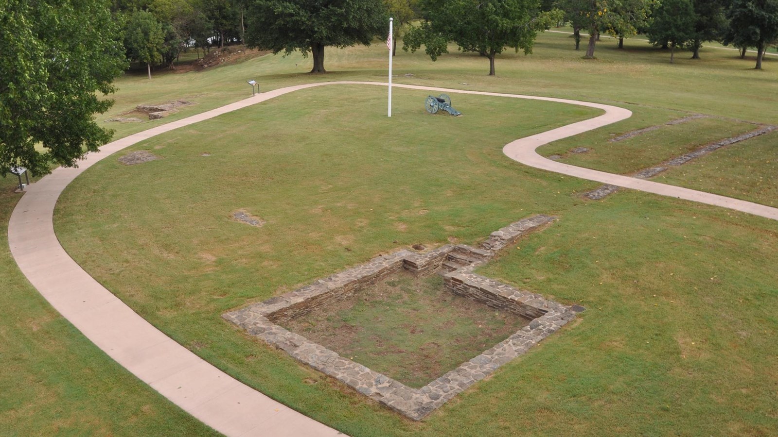 Cement sidewalk winding around flagstone founadtion. Blockhouse foundation in lower right.