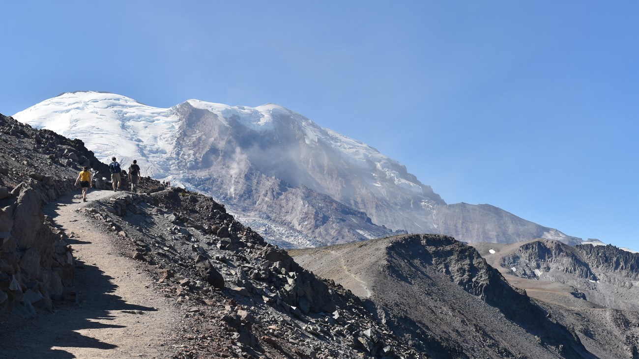 View of glaciated mountain from rolling ridgeline with three rocky peaks.