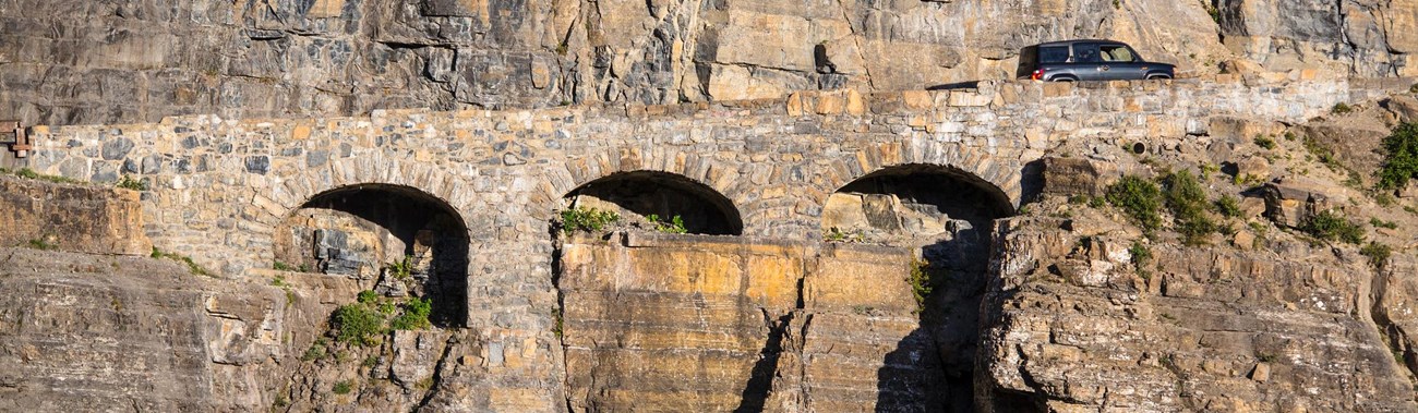 Car drives uphill over triple arched stone bridge