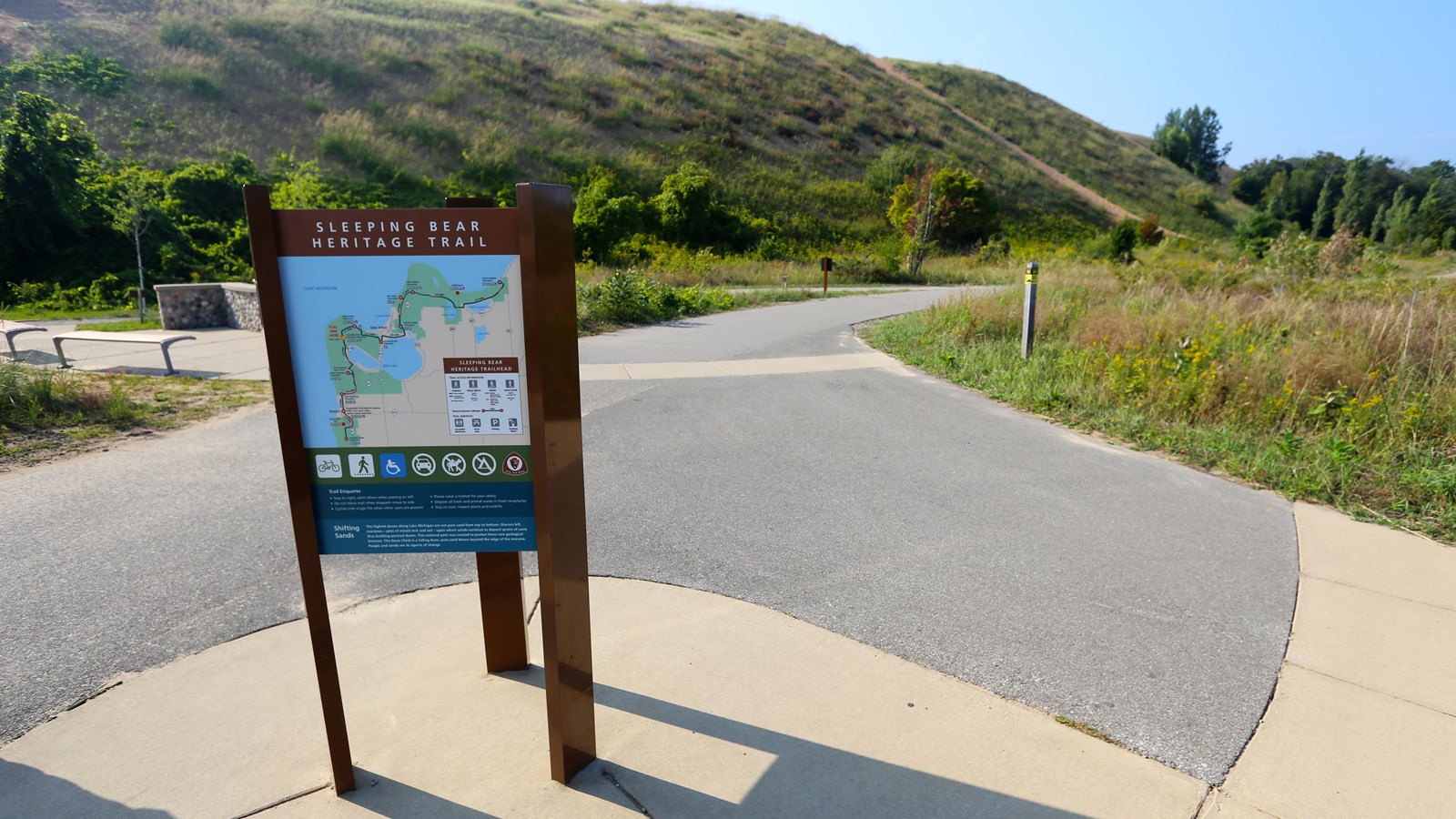 Sign with trail information stands at corner of parking lot and paved trail.