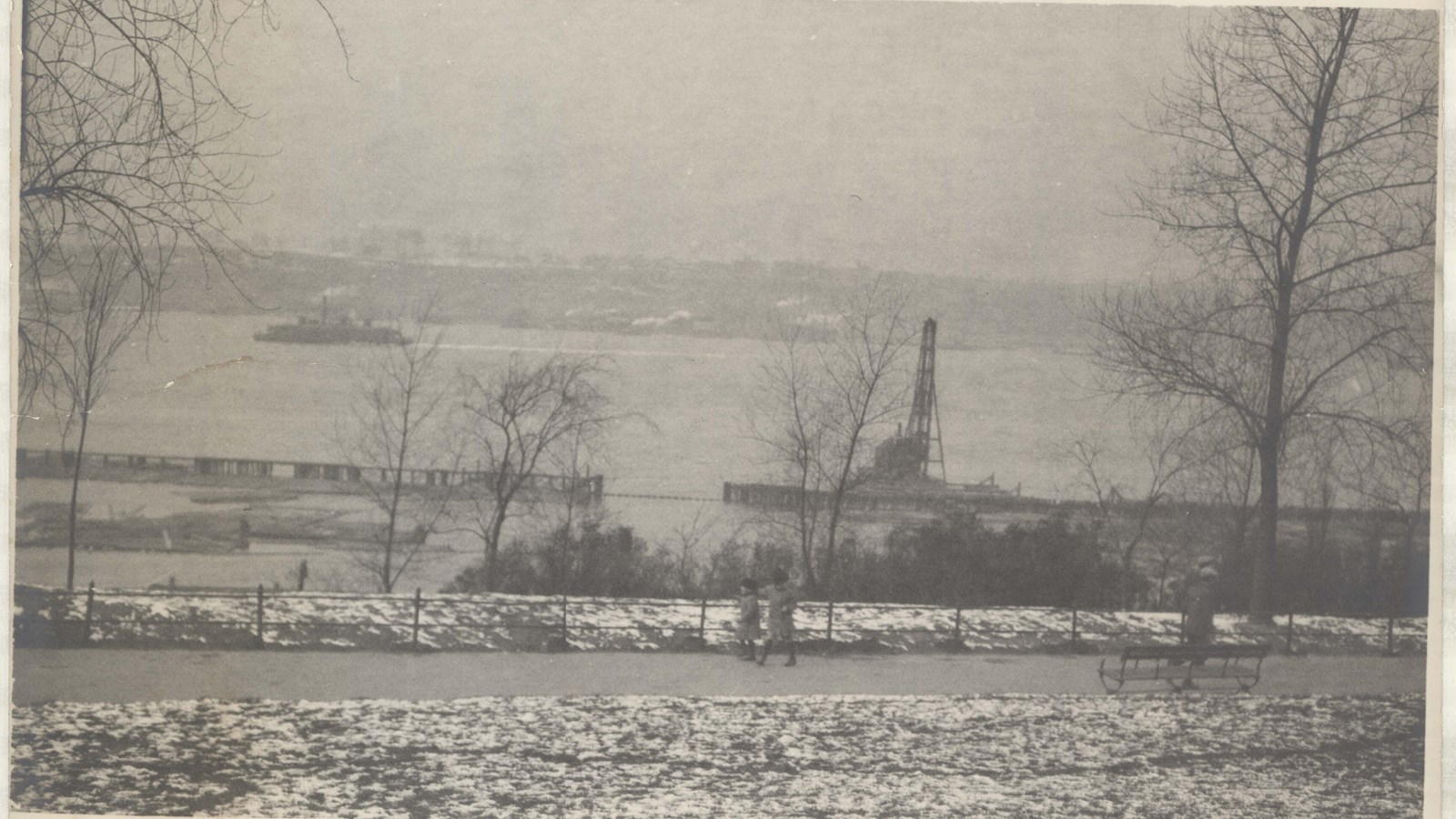 Black and white path with people walking along, snow on both sides, water below path 