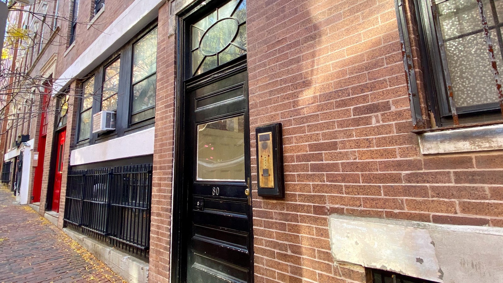 Exterior of a brick building with a black door and an apartment callbox to the right. 