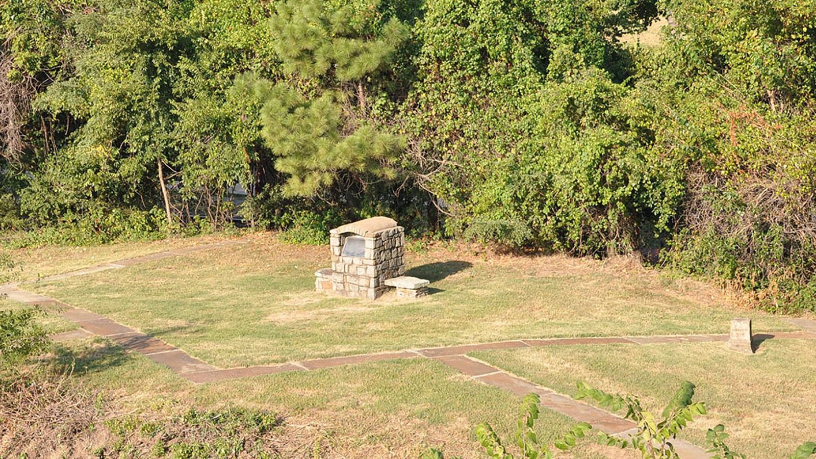 Aerial view flagstone foundation ouline, stone mounment, and stone cube surrounded by grass.