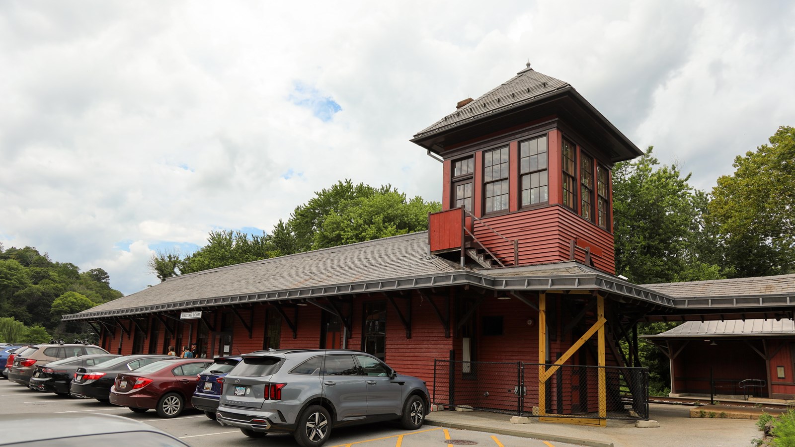 A large red building with a tower on the right side. Cars line up in front of the building. 
