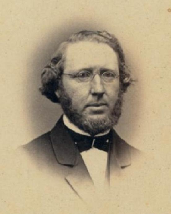 Portrait of a man with round beard, circular glasses, and a suit and tie.