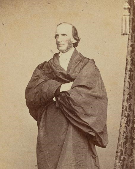 Sepia portrait of a man in a cloak standing with his arms crossed. 