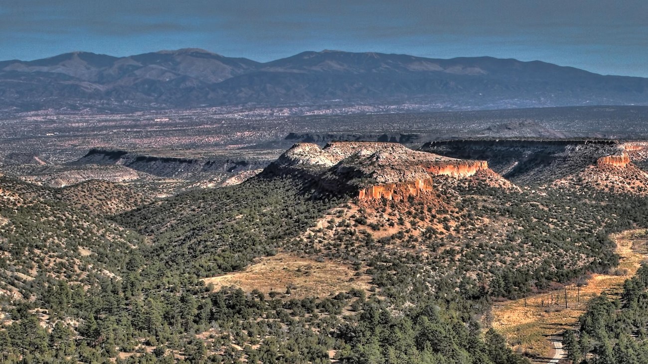 A panoramic view shows mesas dotted with vegetation and mountains in the background.