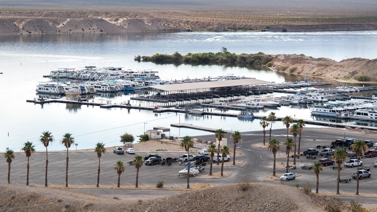 A birds eye view looking down at a marina, palm trees, large body of water, and mountains