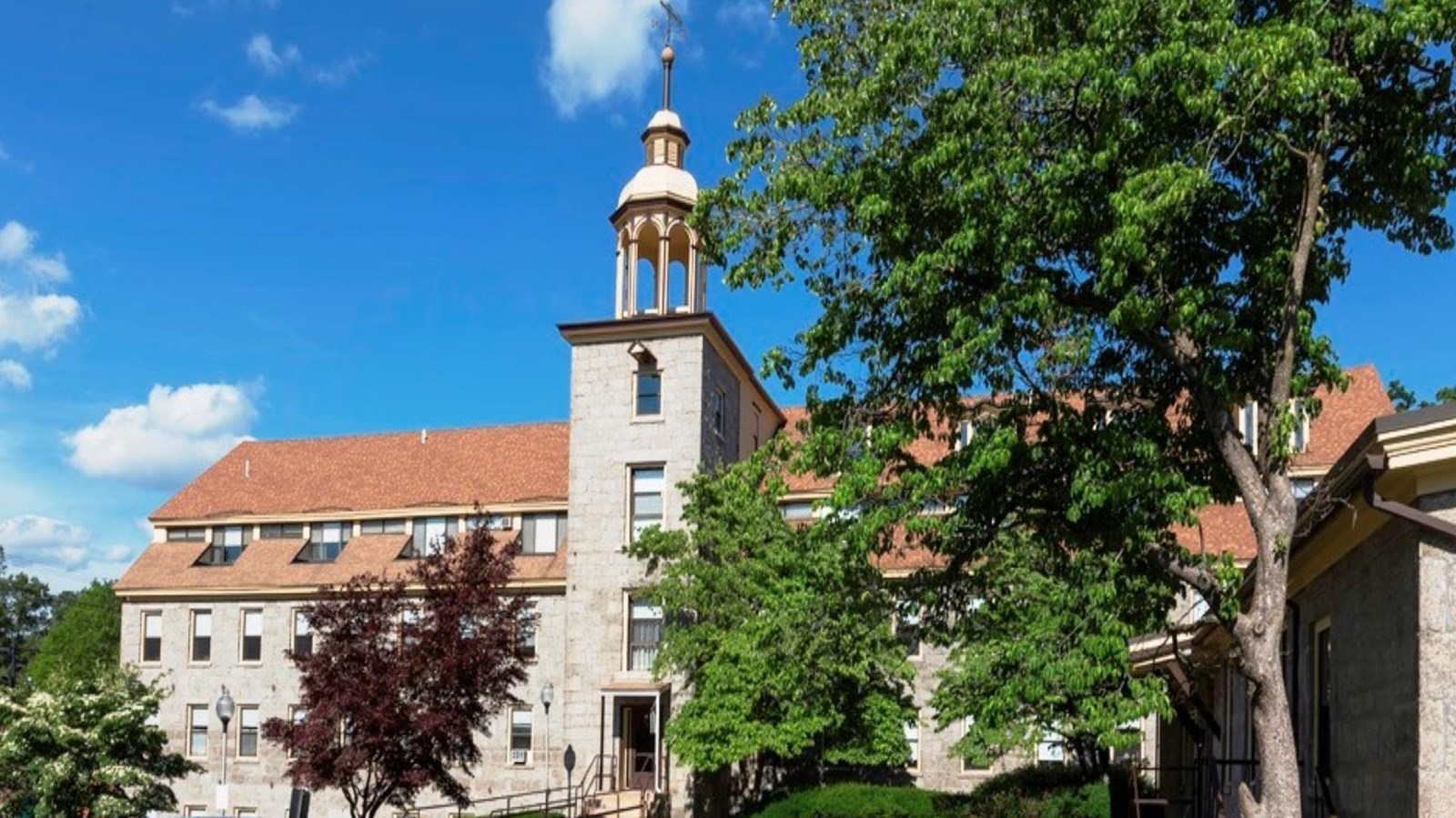 Granite mill in background with bell tower and blue and red car in the foreground and tree