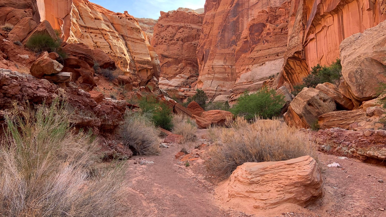 A dry gravel wash flanked by boulders with red and white cliffs rising on either side