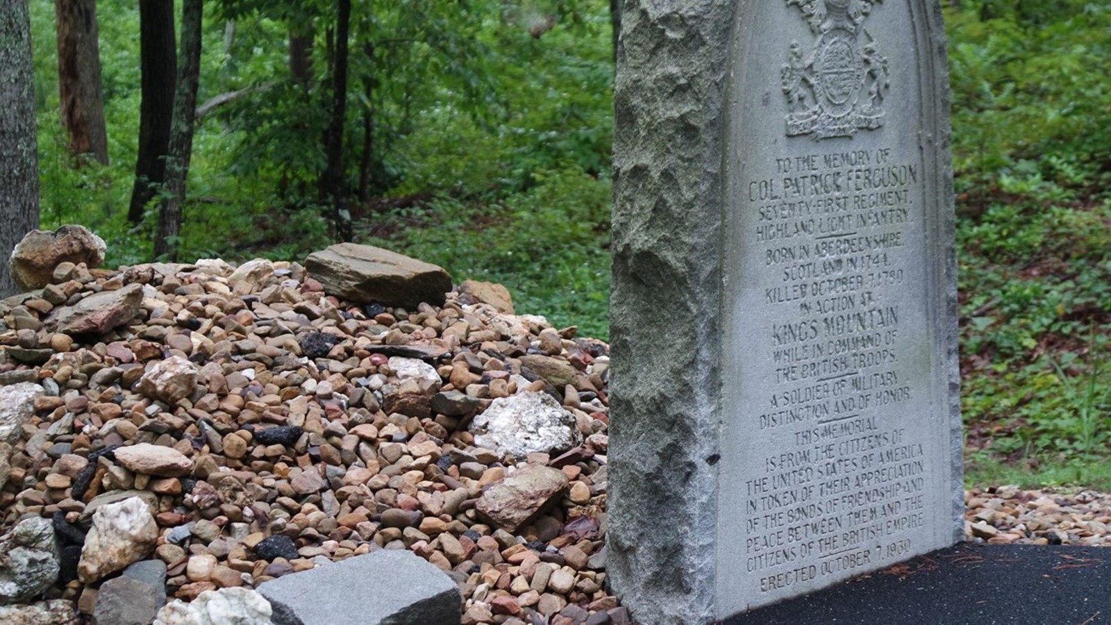 A gravestone with a lot of rocks piled behind it.