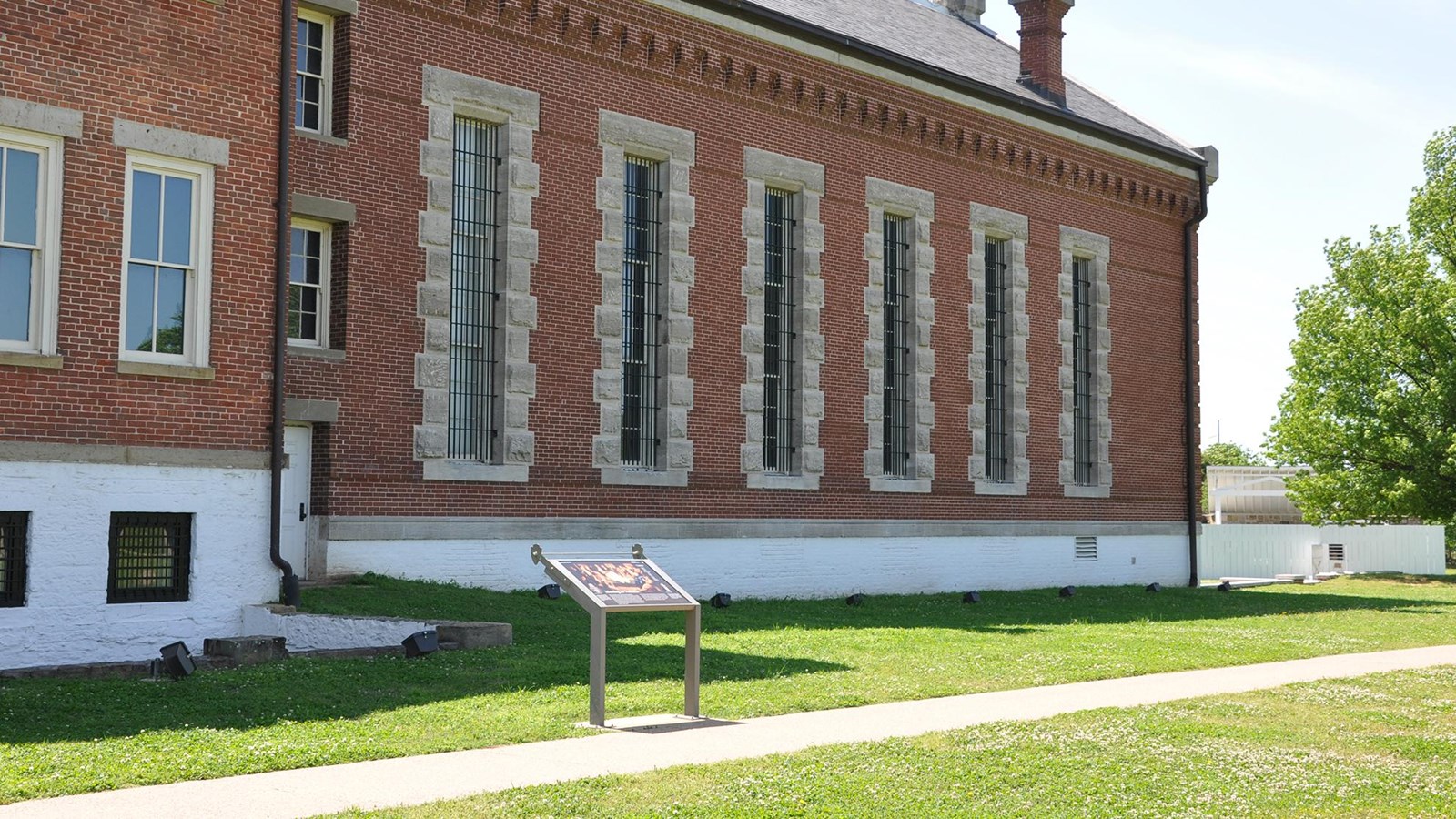 Wayside panel next to a sidewalk, 10 feet from the side of the red brick visitor center.