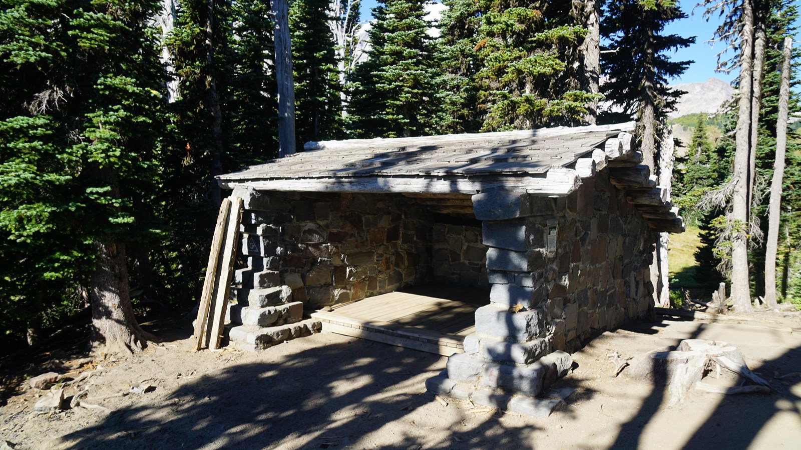 Wooden trail shelter surrounded by trees and subalpine maedow