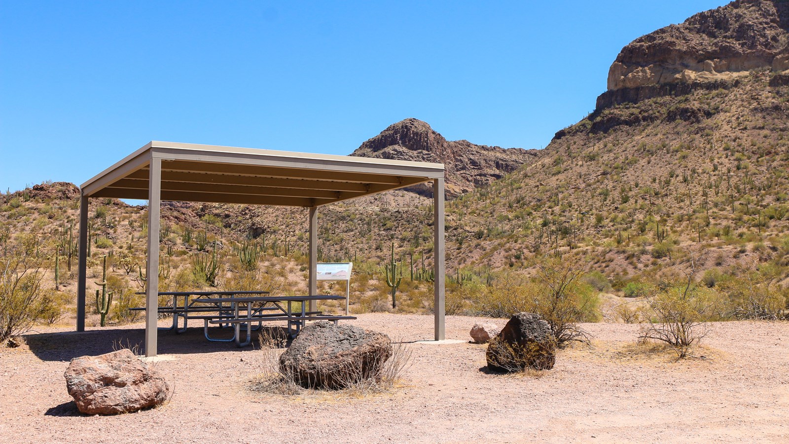 Shaded picnic table and wayside sign sits on the edge of a Diablo wash, with vegetated mountains