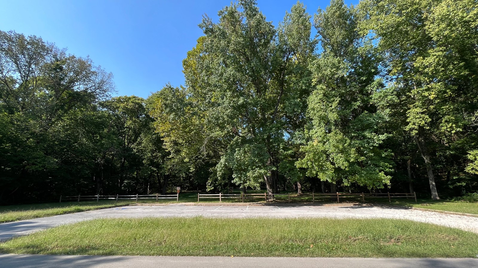 A stone parking area with a patch of grass and trees lining a river bank.