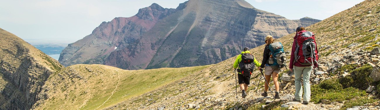 Group of three hikes subalpine trail toward large mountain