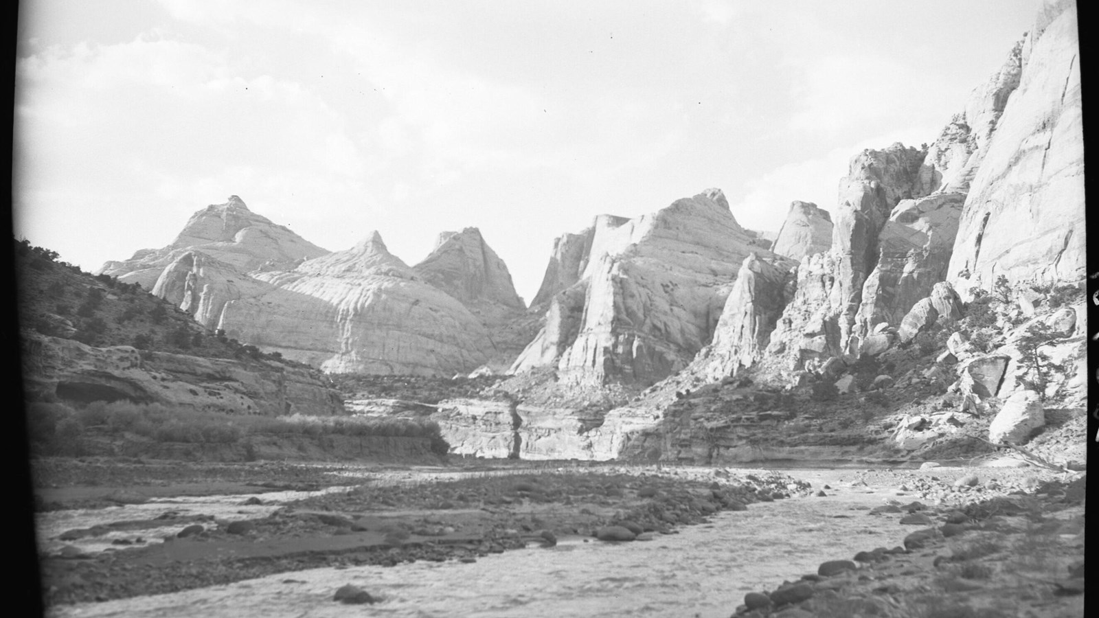 Wide, winding river with boulders in it, little vegetation, and large sandstone domes in background