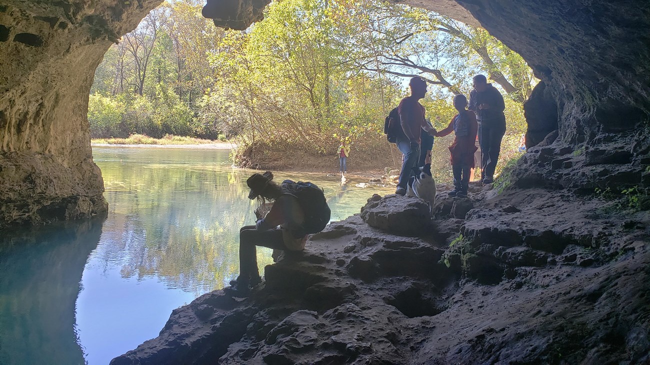 looking out of a gray rock cave, blue water in the cave and in the distance, hikers on rocks of cave