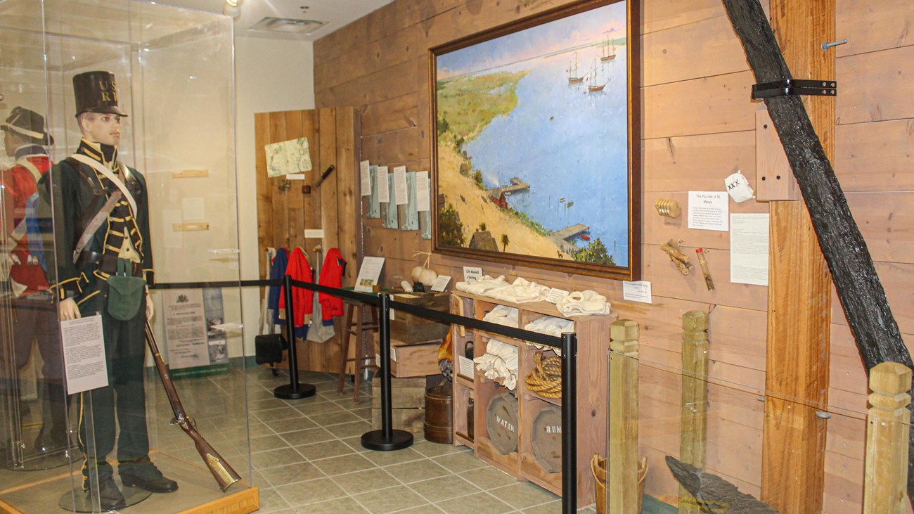 A museum display with manikins in uniforms, a historic painting and a large anchor on the wall. 