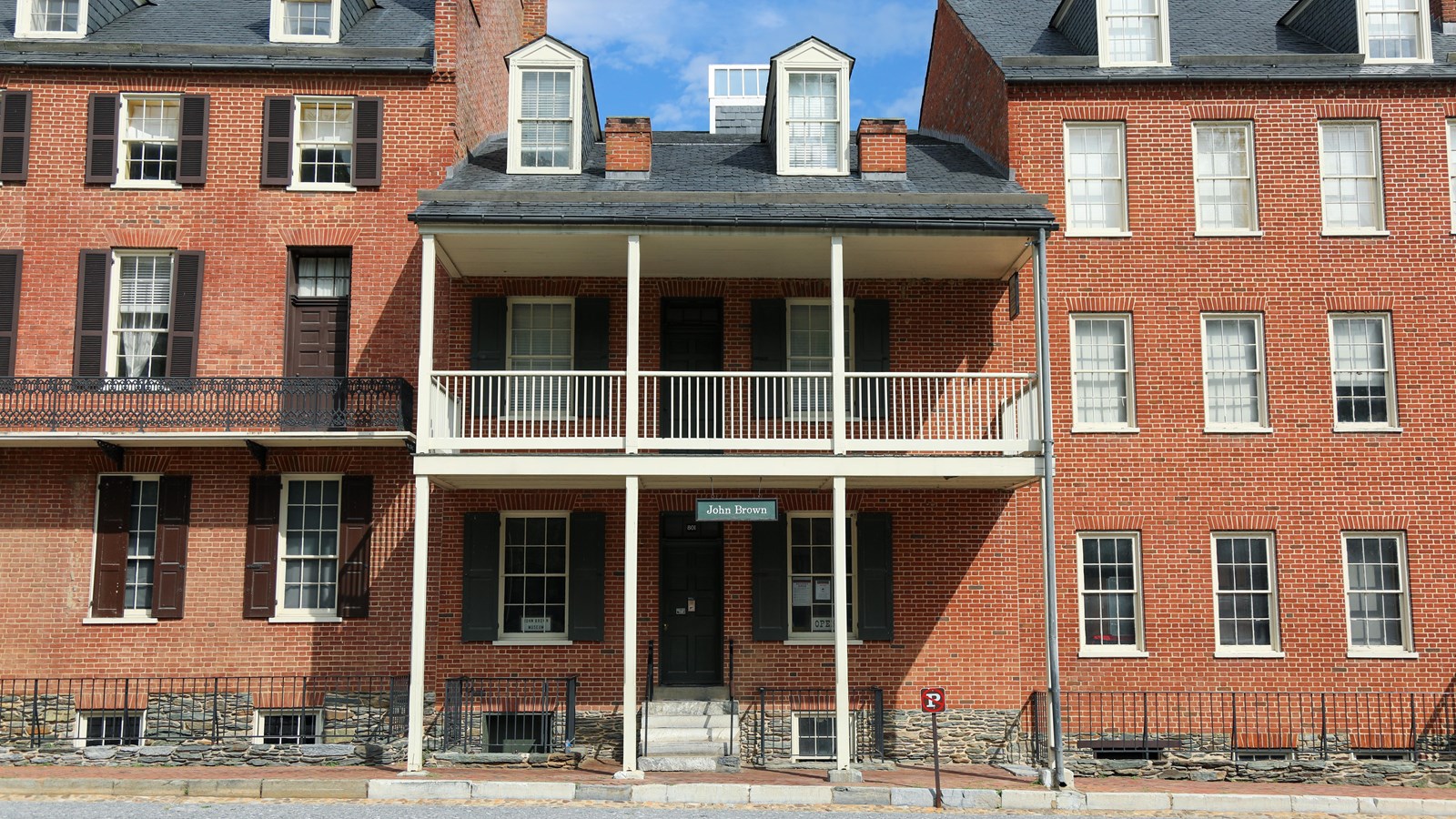A brick rowhouse with balcony flanked by two taller rowhouses.