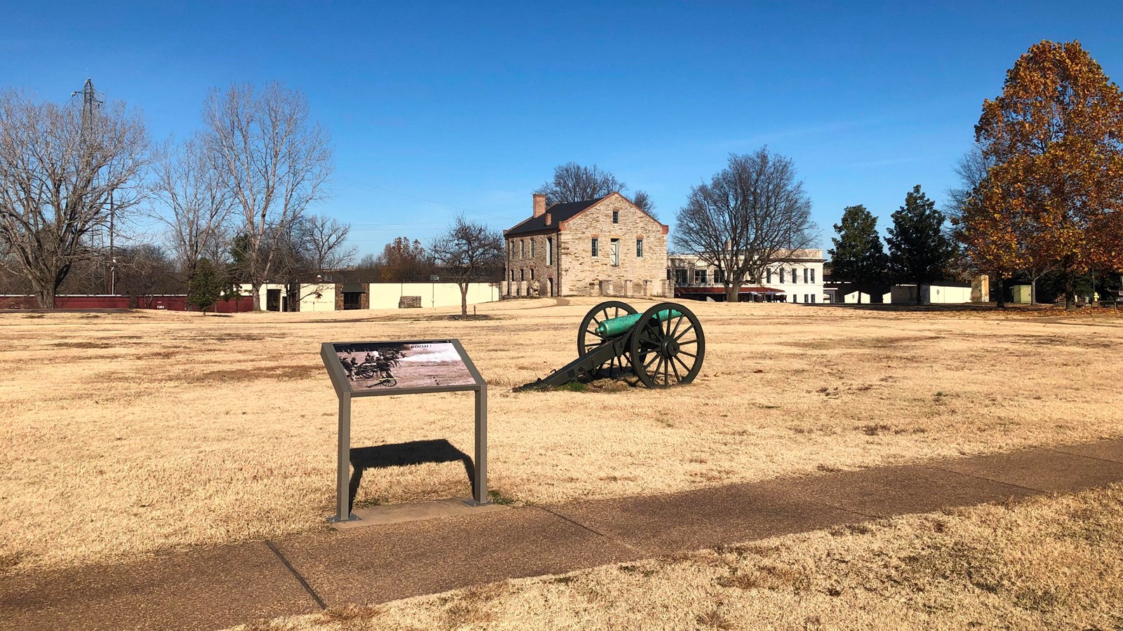 Wayside panel near a cannon and stone commissary building in background. On a clear winter day.