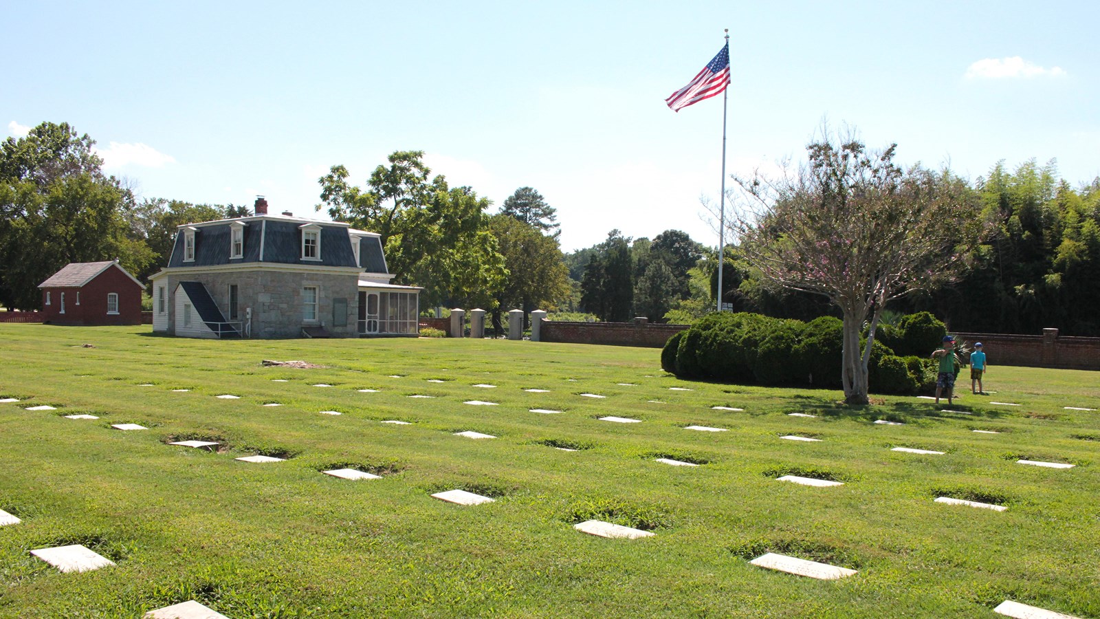 A grey house is in the background with an American Flag on a pole.  Grave markers are in foreground