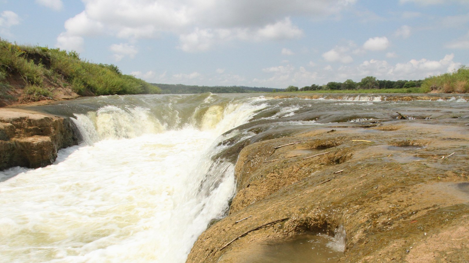 A waterfall in the middle of a river drops off about 5 feet with stone ledges on both sides.