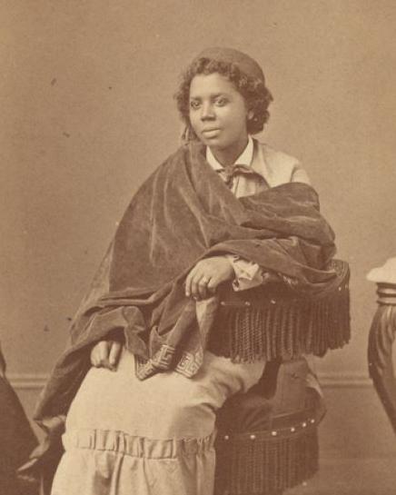 Studio portrait of Edmonia Lewis seated and wearing a beret with a shawl over her top and long skirt