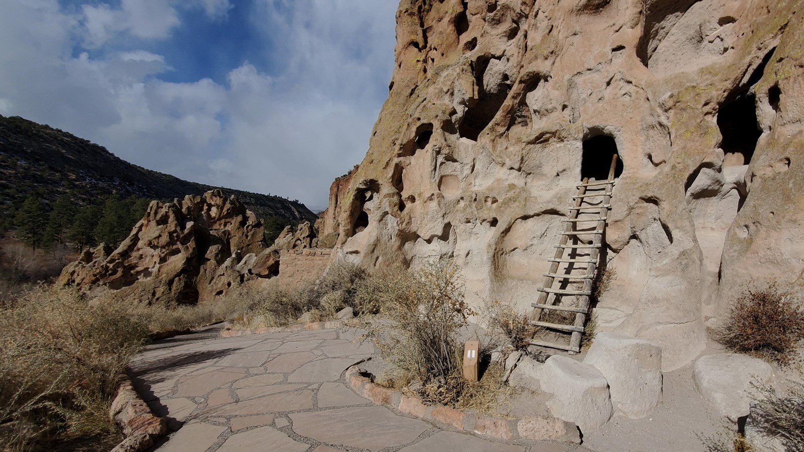 a wooden ladder leans against an opening in a cliff of tan stone while a path passes by