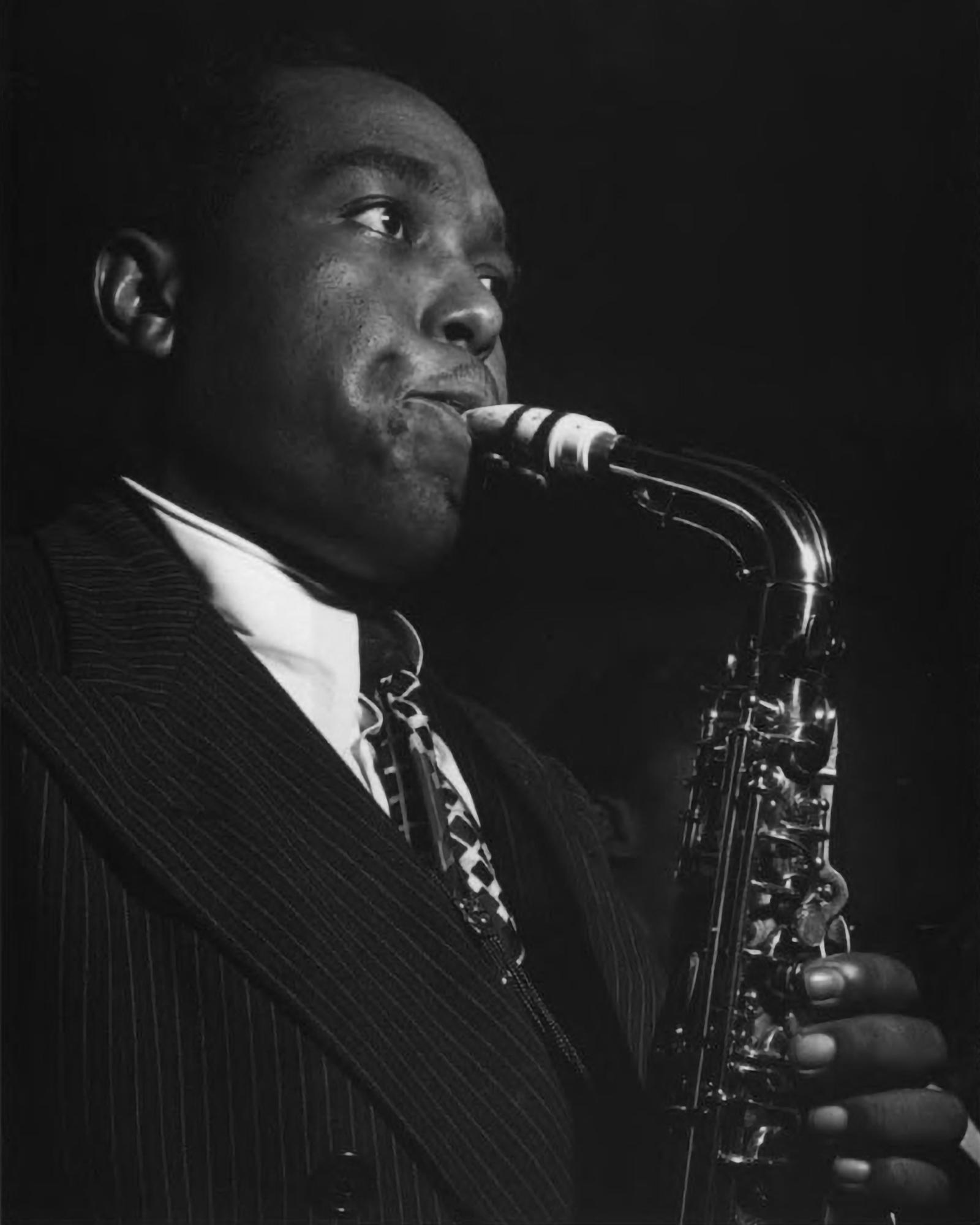 Head and shoulders of man in suit blowing into saxophone in dimly lit room