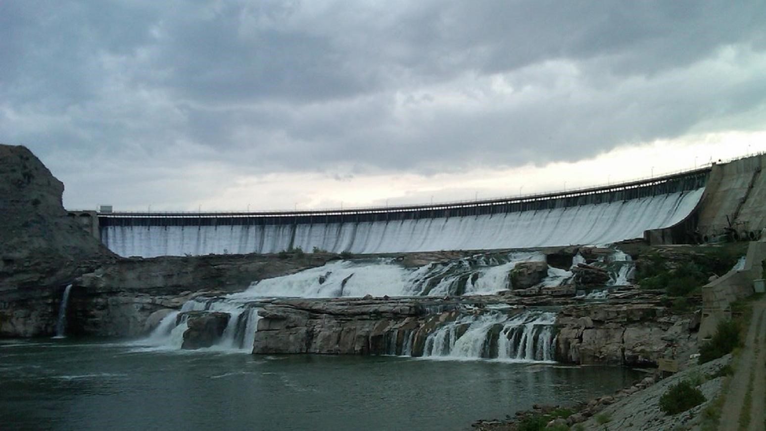 Water cascades down the wall of a dam and a rocky shelf