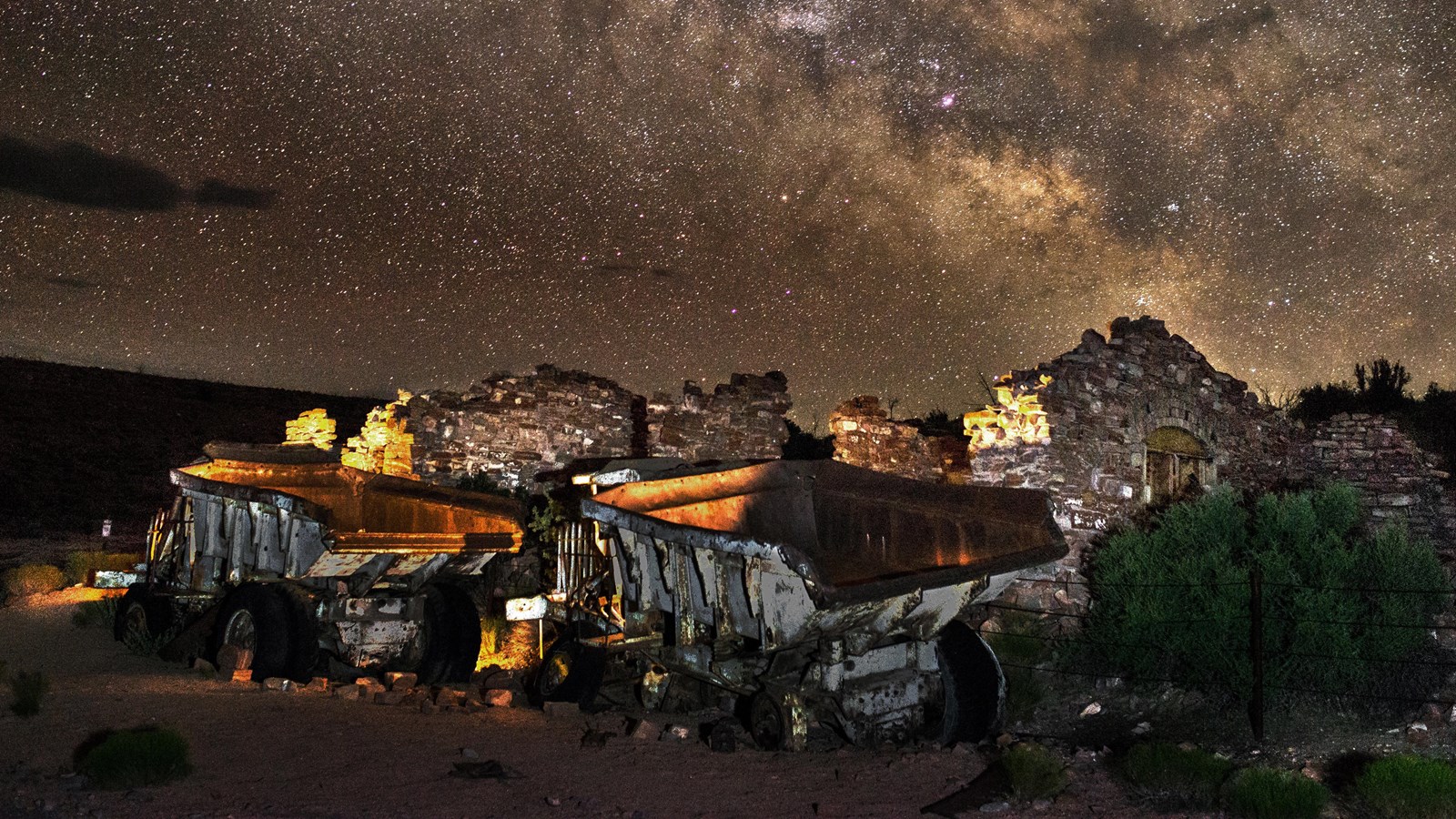 Old mining trucks with an amber glow set in front of a starry night sky.