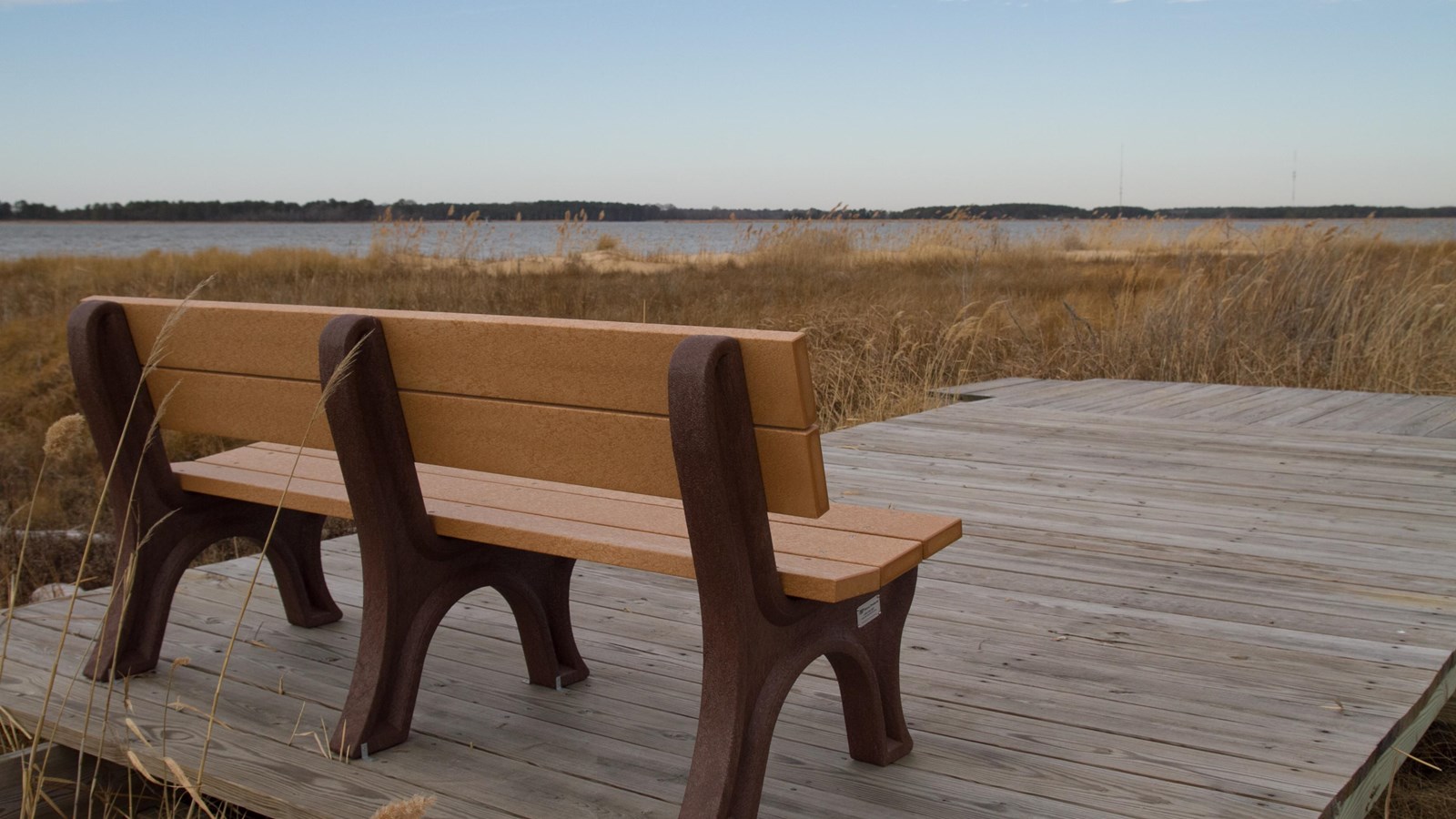 Bench on a raised wooden platform overlooking browned marshland in winter