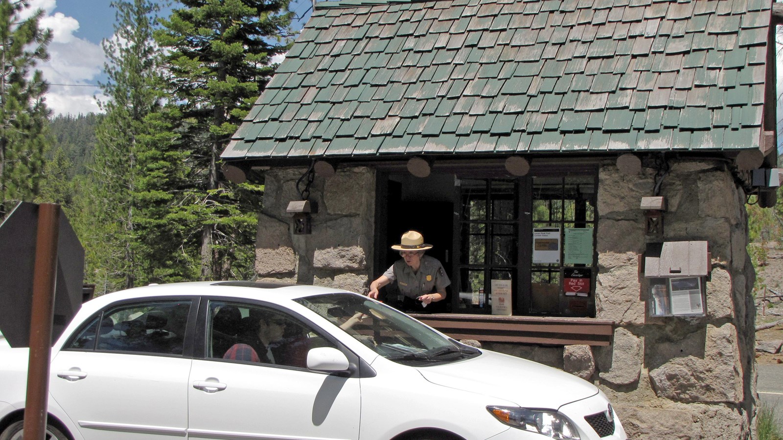a park ranger hands a park map from a fee booth to visitors in a white car