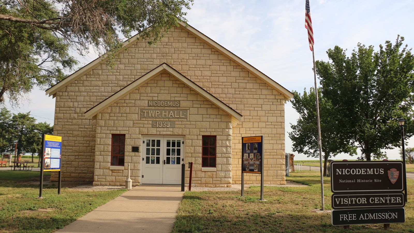 Sidewalk leads to limestone building with white double doors and frame windows.