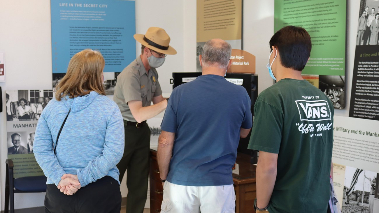 A ranger in a flat hat presents information to three visitors.