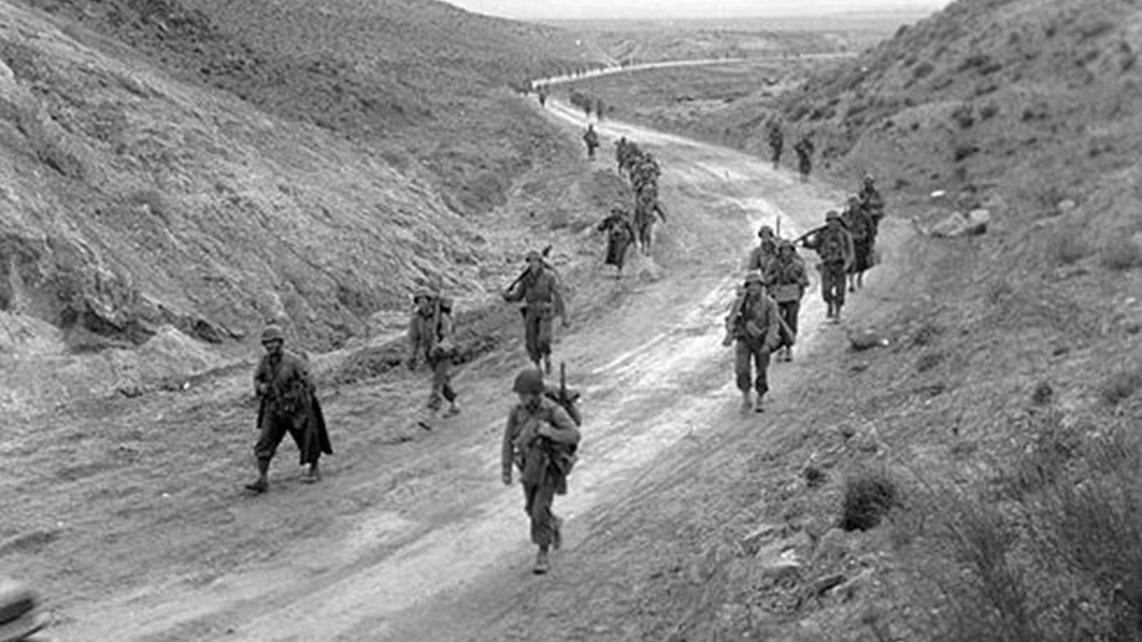 Uniformed men marching across sandy terrain.